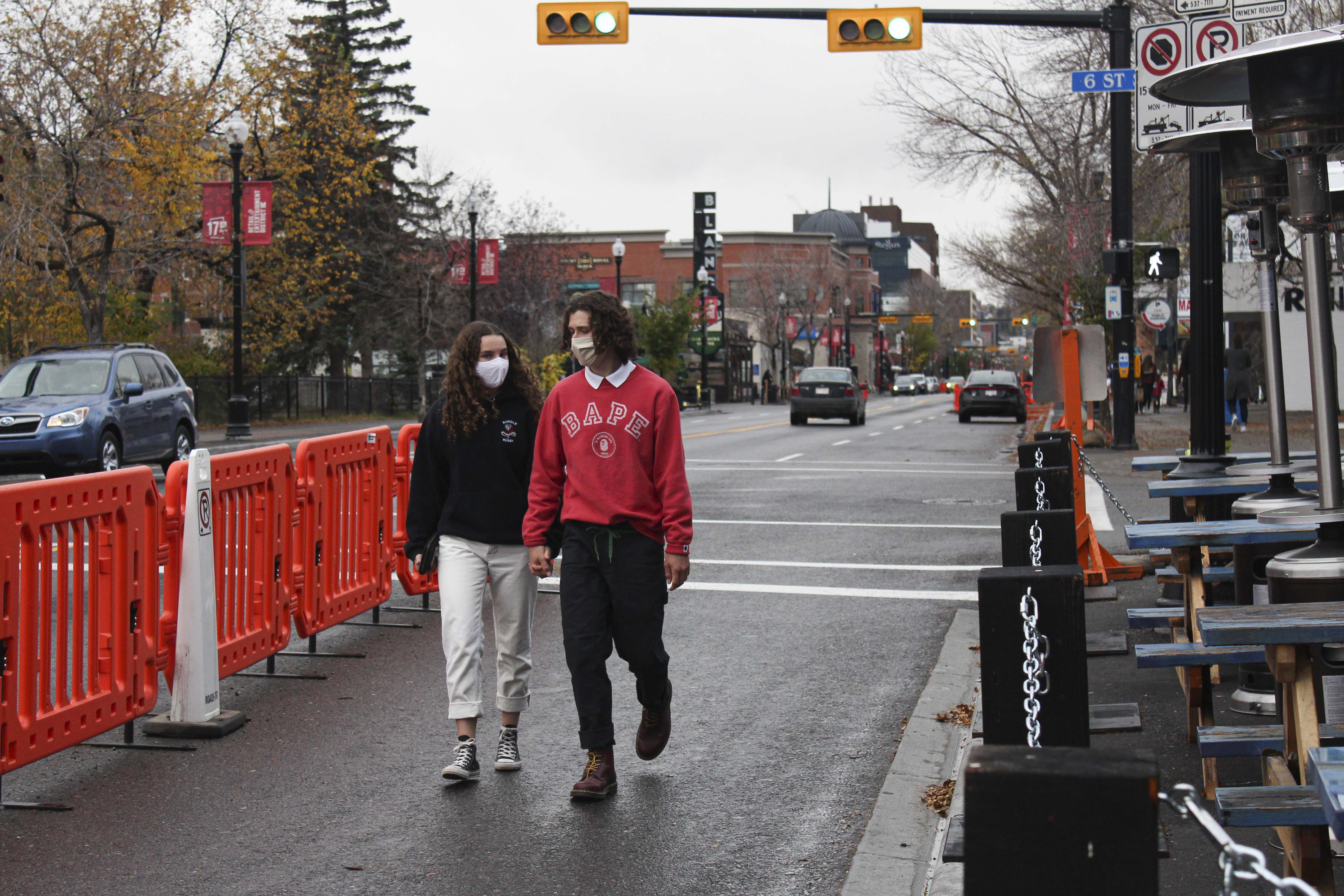 Calgary couple, wearing masks, uses the extended sidewalk for social distancing on 17th Ave in downtown Calgary on Monday, Oct. 12, 2020. The city allows restaurants to use the sidewalk for extra outdoor space in order to help stopping the spread of COVID-19 virus. (Photo by Meng Wei/SAIT)